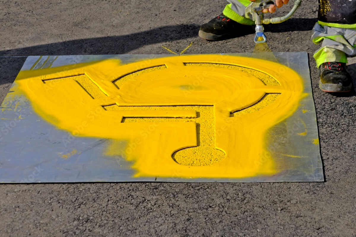 Yellow handicap accessibility stencil being painted on asphalt pavement